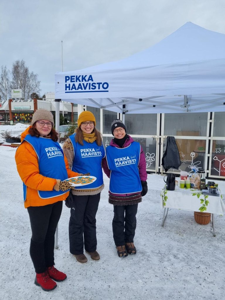 Kolme Pirkkalan Vihreiden edustajaa tukemassa Pekka Haaviston kampanjaa torilla, jossa katos ja luminen ympäristö.